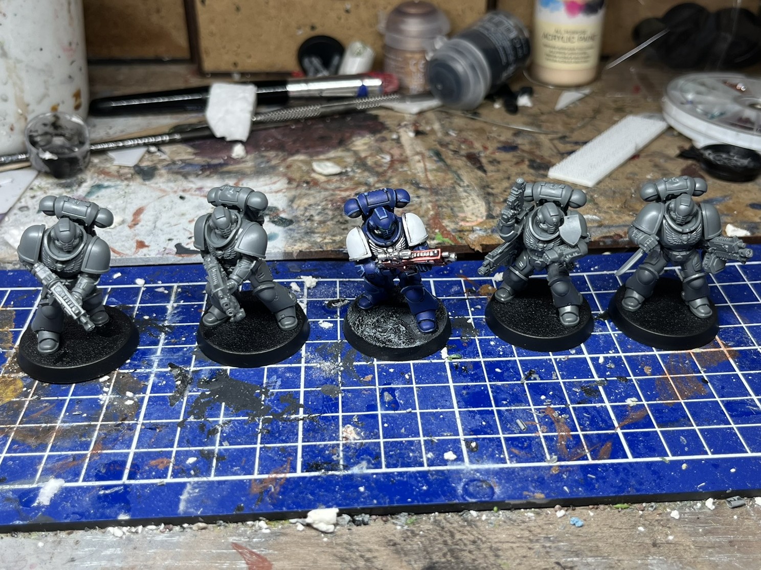 Photograph of a set of 5 28mm space marine. One of the models is painted and the other 4 are grey plastic.